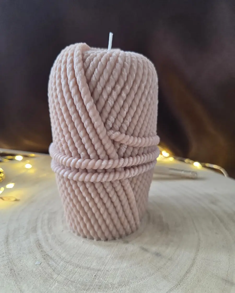 Pale pink candle shaped like a wound ball of rope, fairy lights behind
