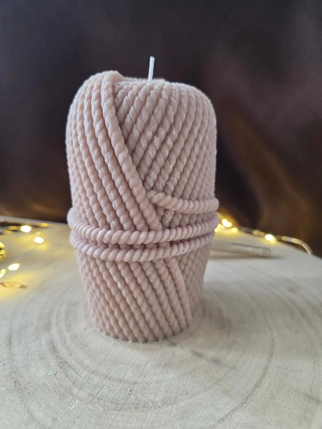 Pale pink candle shaped like a wound ball of rope, fairy lights behind