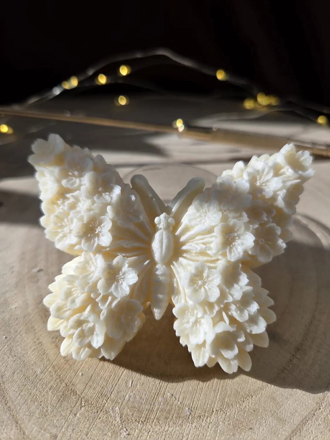 Ivory butterfly candle with wings made of small moulded flowers, in low sunlight