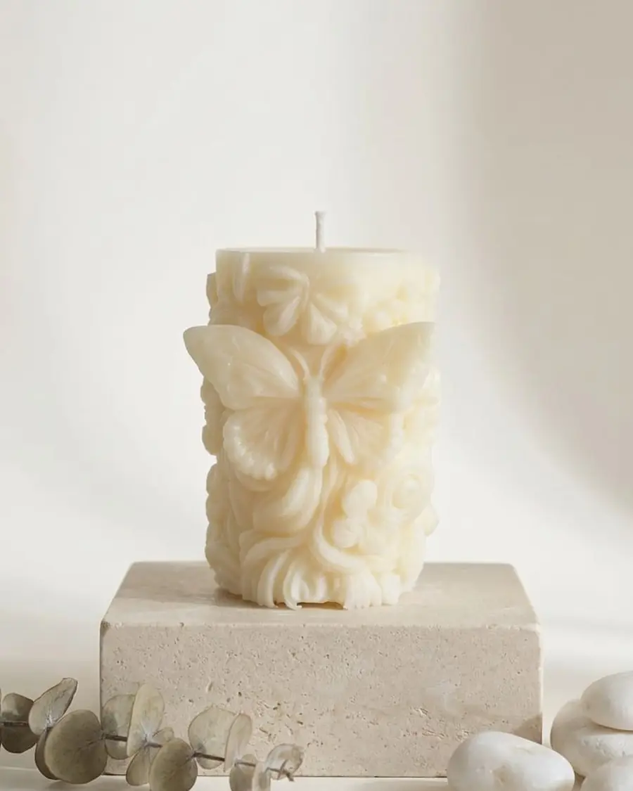 Ivory pillar candle with a butterfly and flowers, on a stone block with eucalyptus