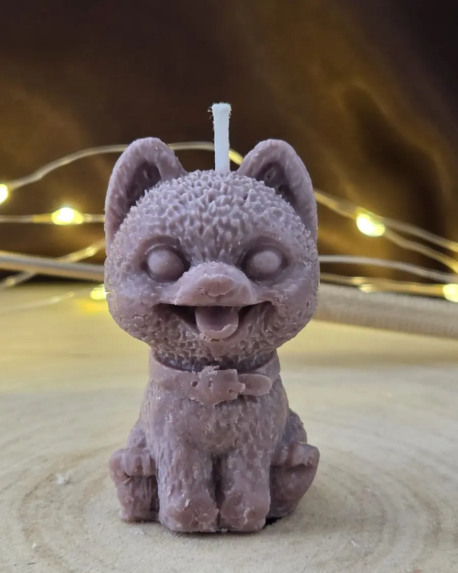 Mauve cat candle with its tongue out and a buckled collar, on a wood slice