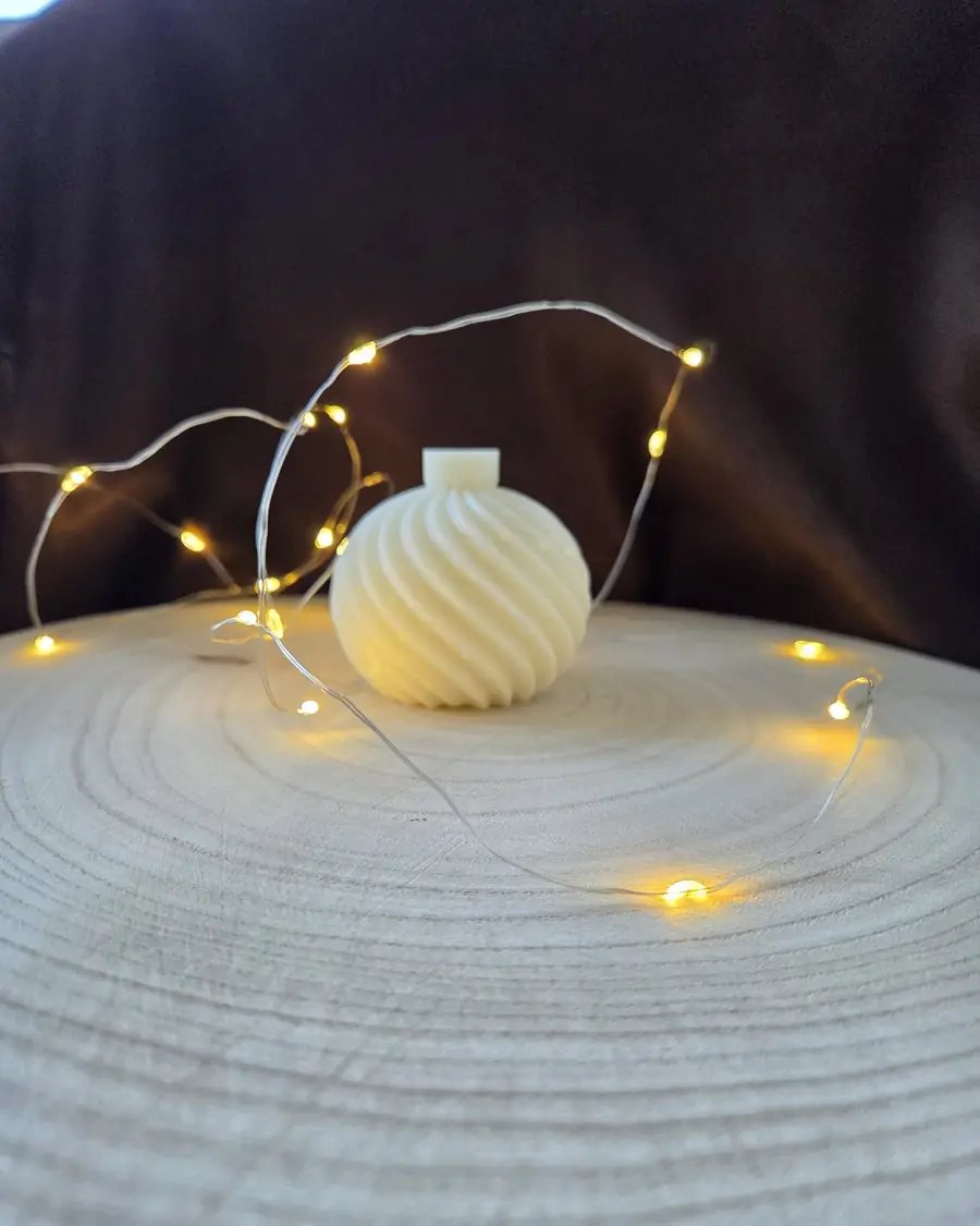 Ivory swirled bauble candle on a wood slice circled by fairy lights