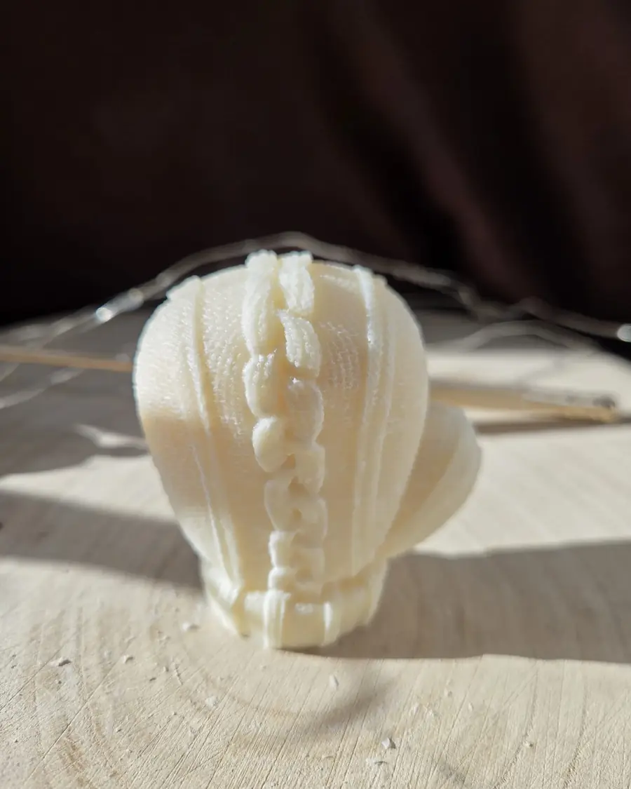 Ivory mitten candle with a cable knit pattern, in low sunlight