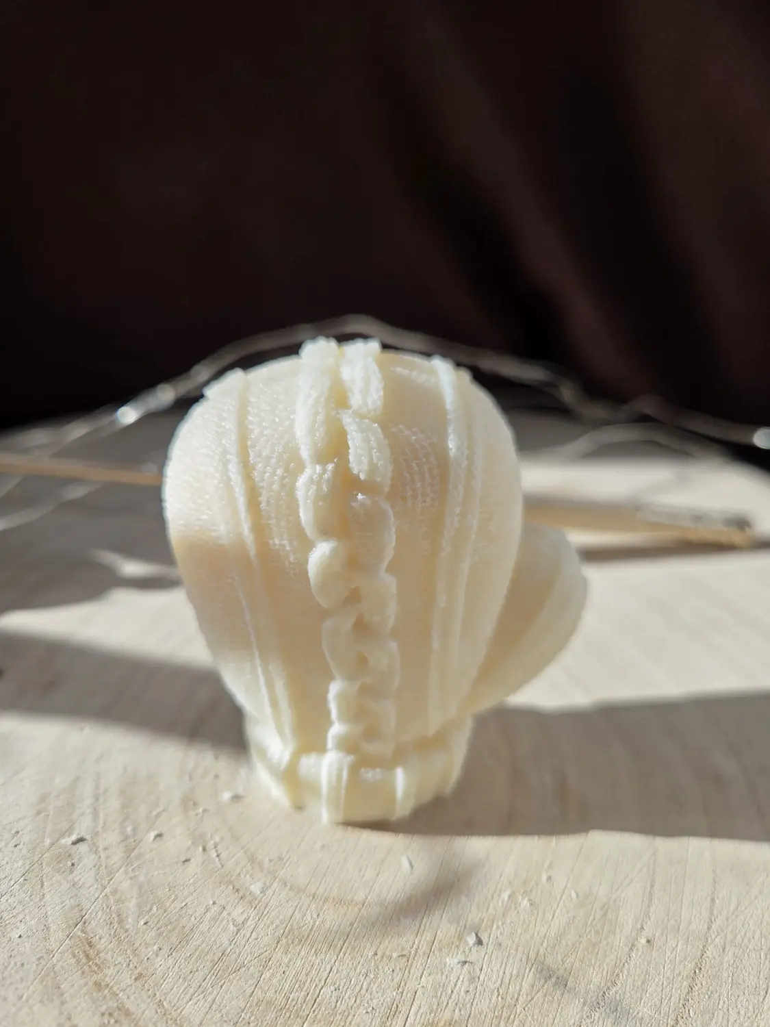 Ivory mitten candle with a cable knit pattern, in low sunlight
