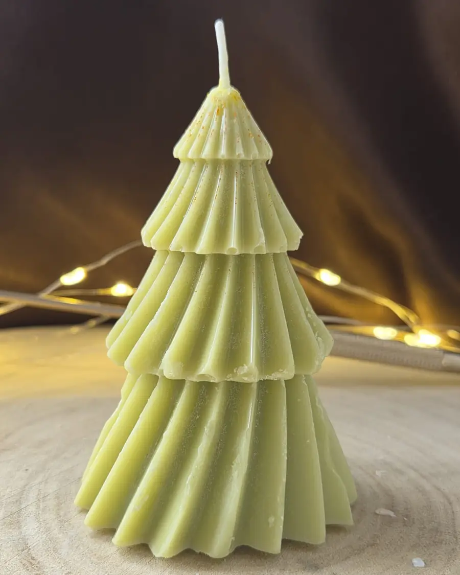 Green tiered Christmas tree candle with gold dust at the top, fairy lights behind
