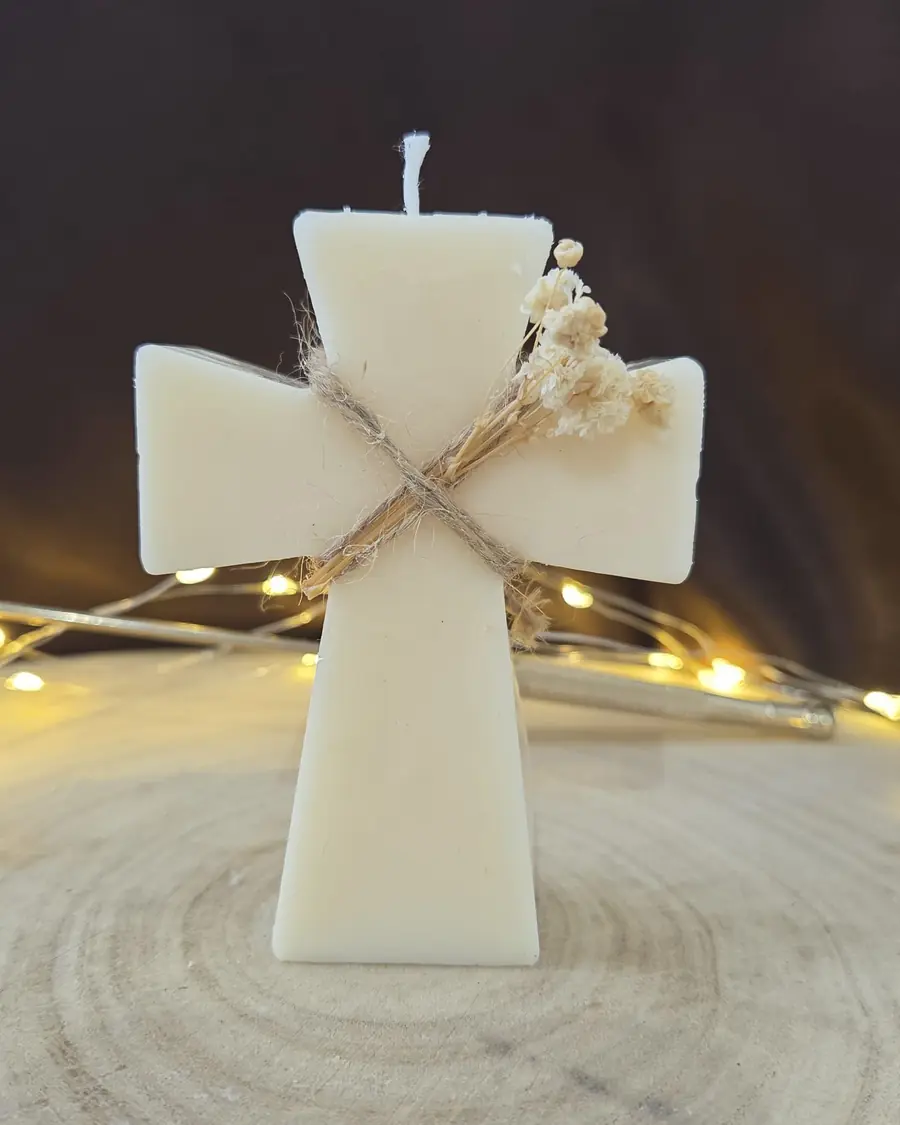 Ivory cross candle tied with twine and a sprig of dried gypsophila, fairy lights behind