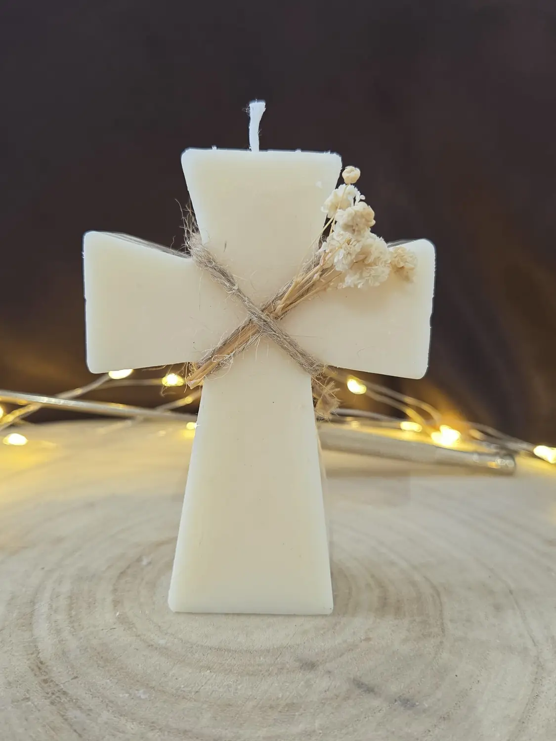 Ivory cross candle tied with twine and a sprig of dried gypsophila, fairy lights behind