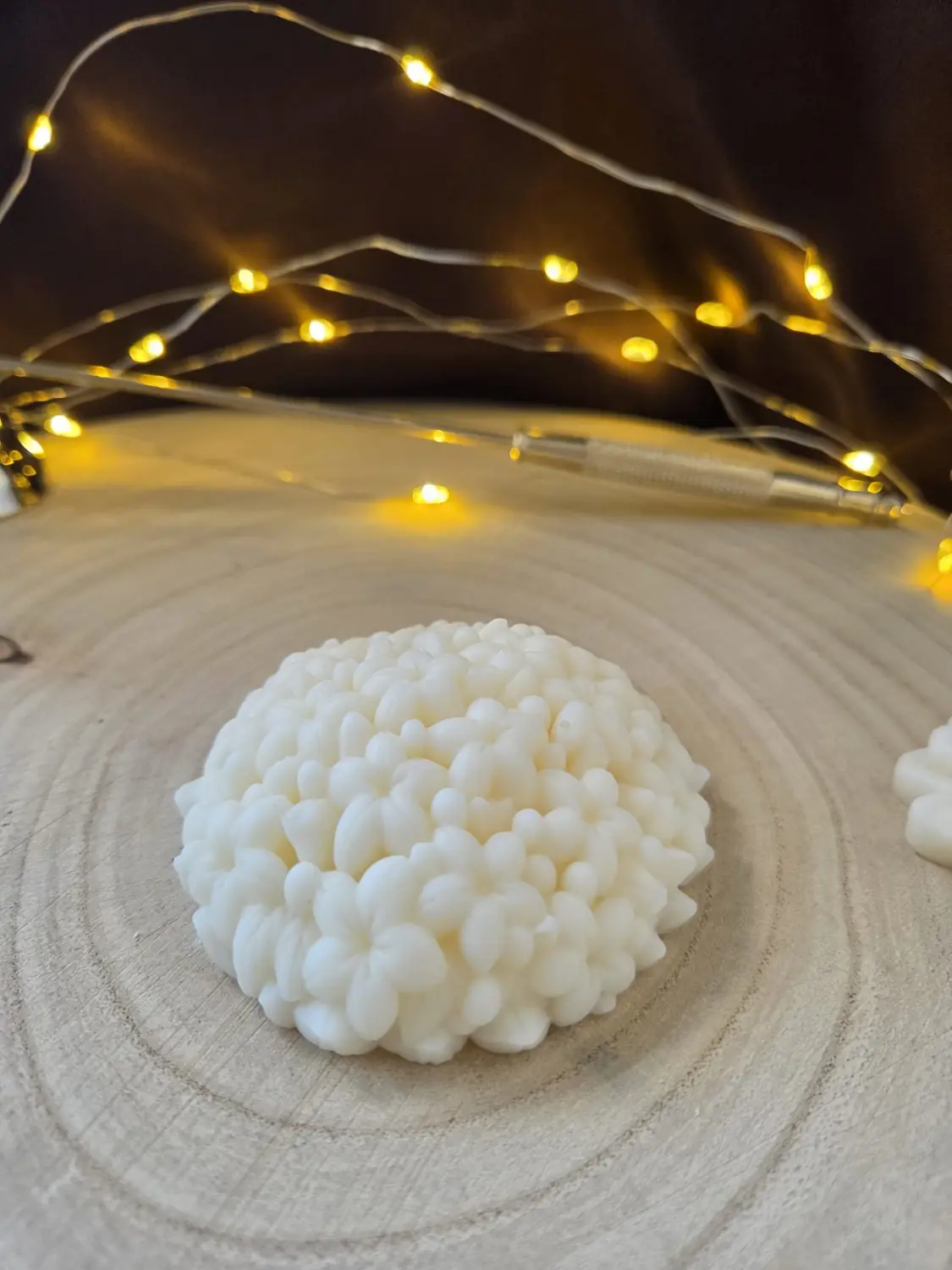 Ivory candle shaped like a dome of tiny flowers, on a wood slice