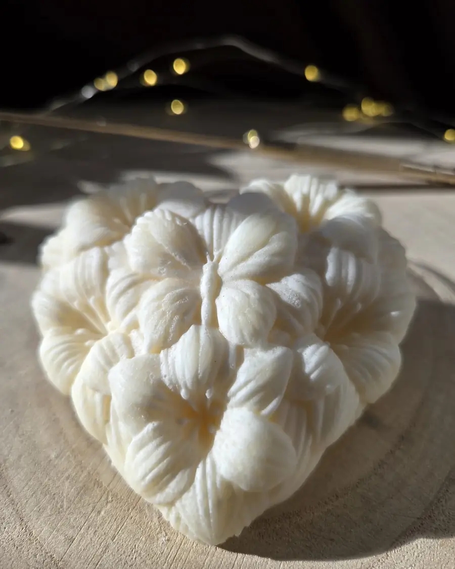 Ivory heart candle made of moulded flowers with a butterfly, in low sunlight