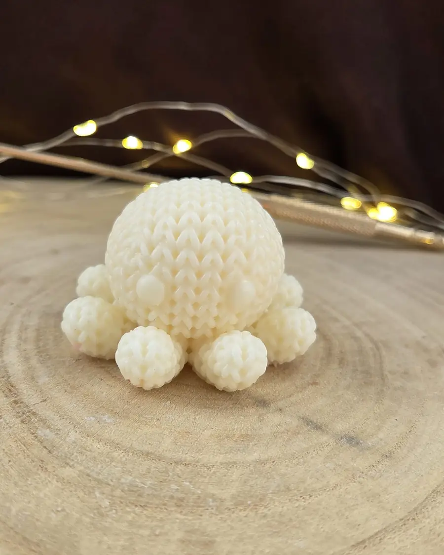 Ivory octopus candle with a knitted texture and bobble legs, on a wood slice