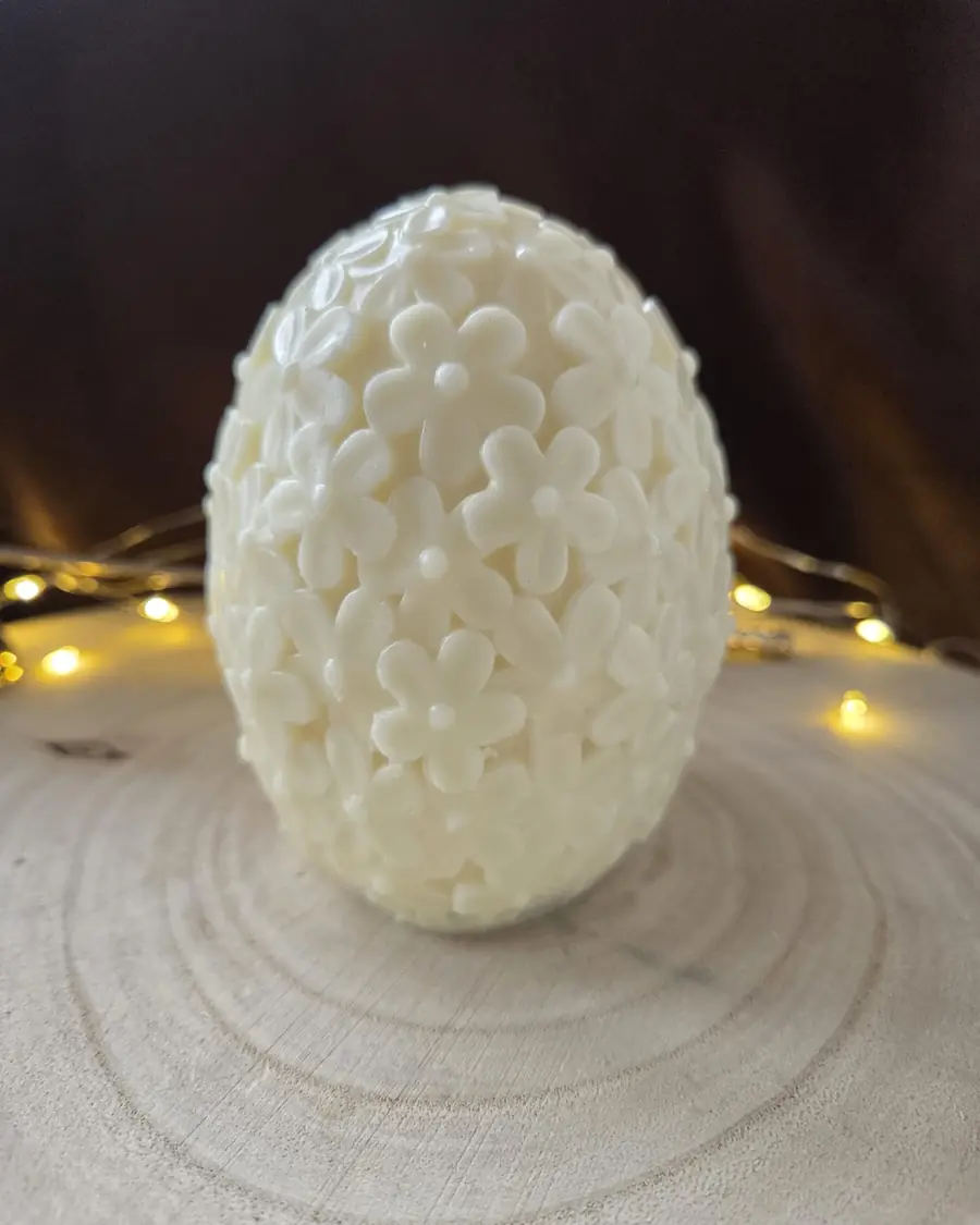 Ivory egg candle covered in small carved flowers, on a wood slice