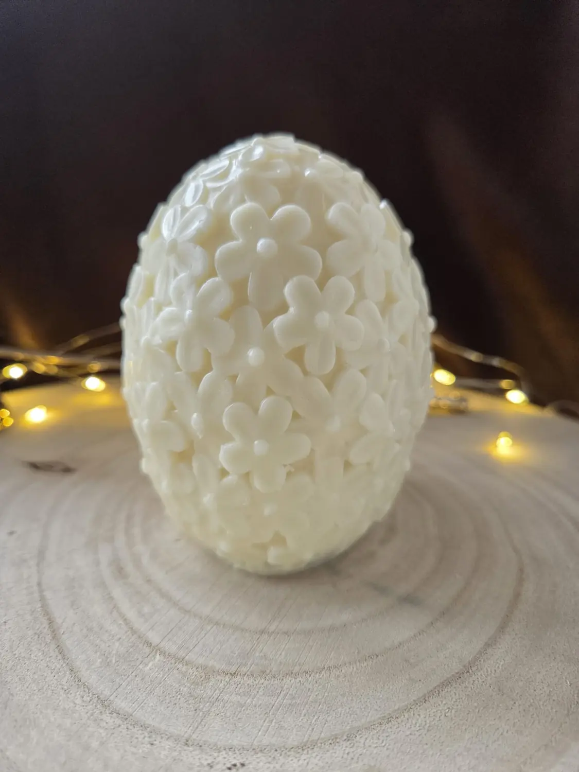 Ivory egg candle covered in small carved flowers, on a wood slice