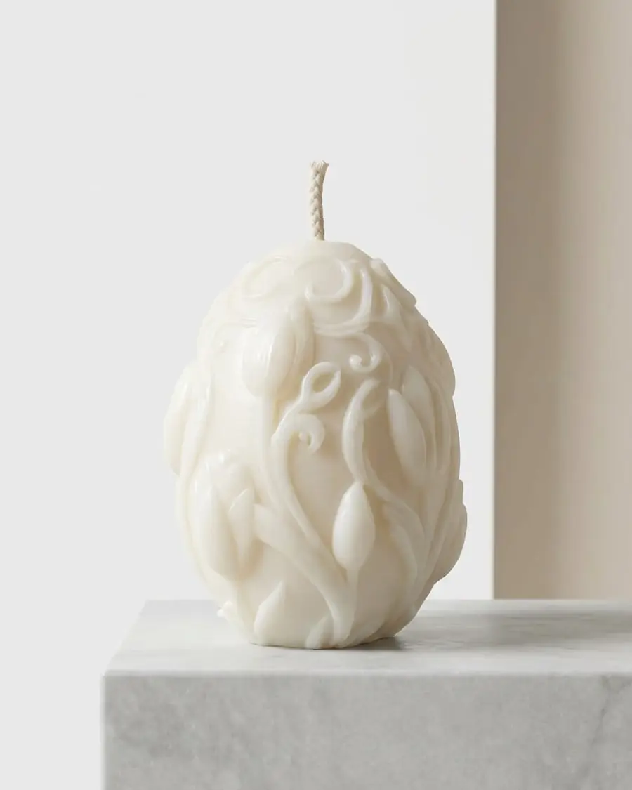 Ivory egg candle carved with swirls and leaves, on a stone block
