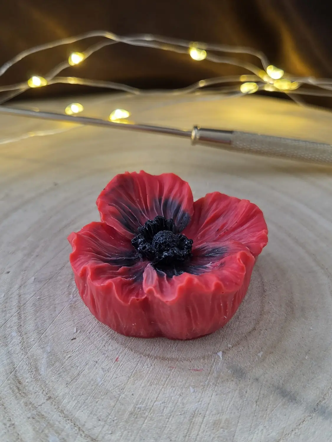 Red poppy candle with a black centre on a wood slice