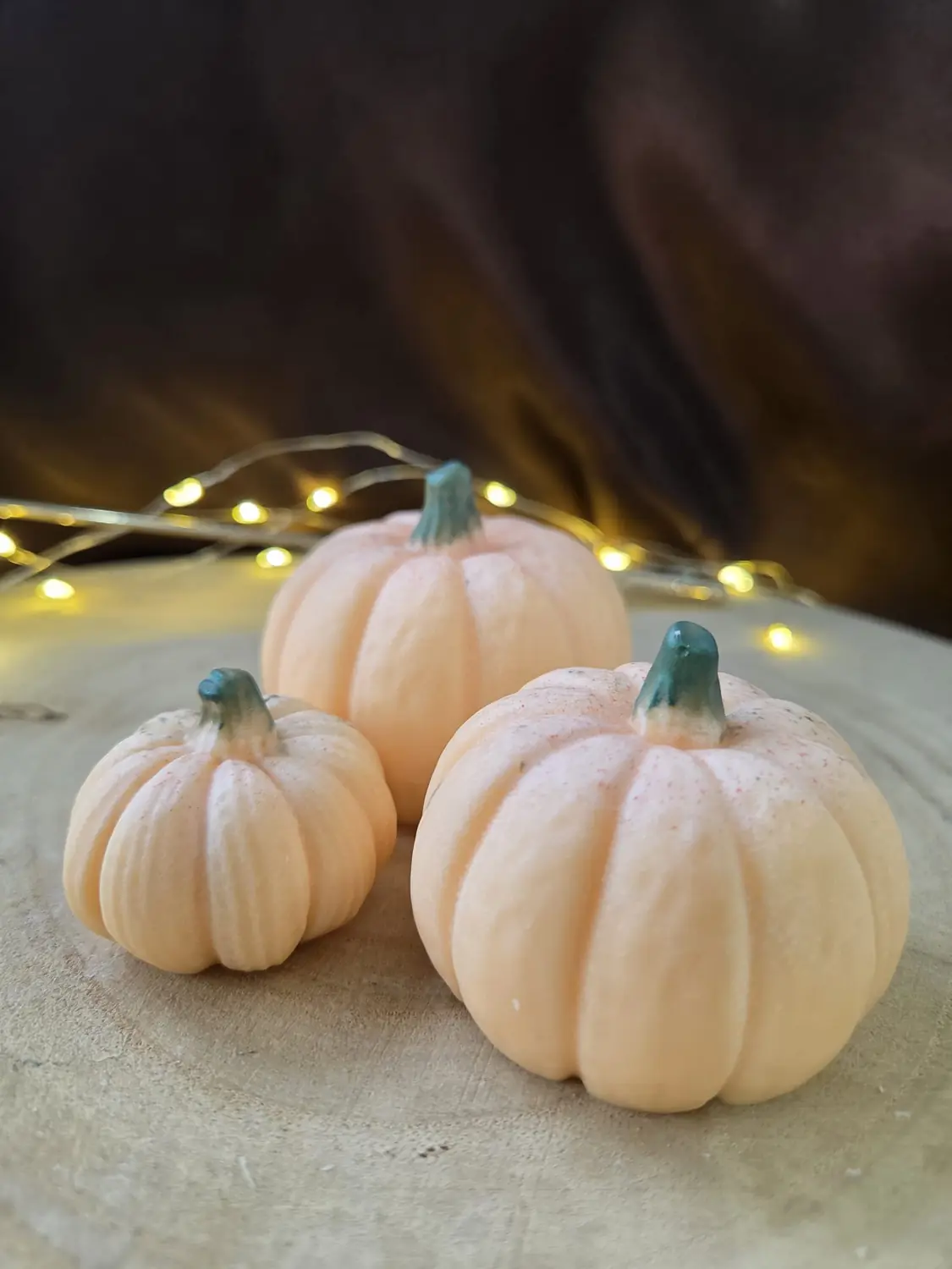 Three soft orange pumpkin candles with green stalks on a wood slice