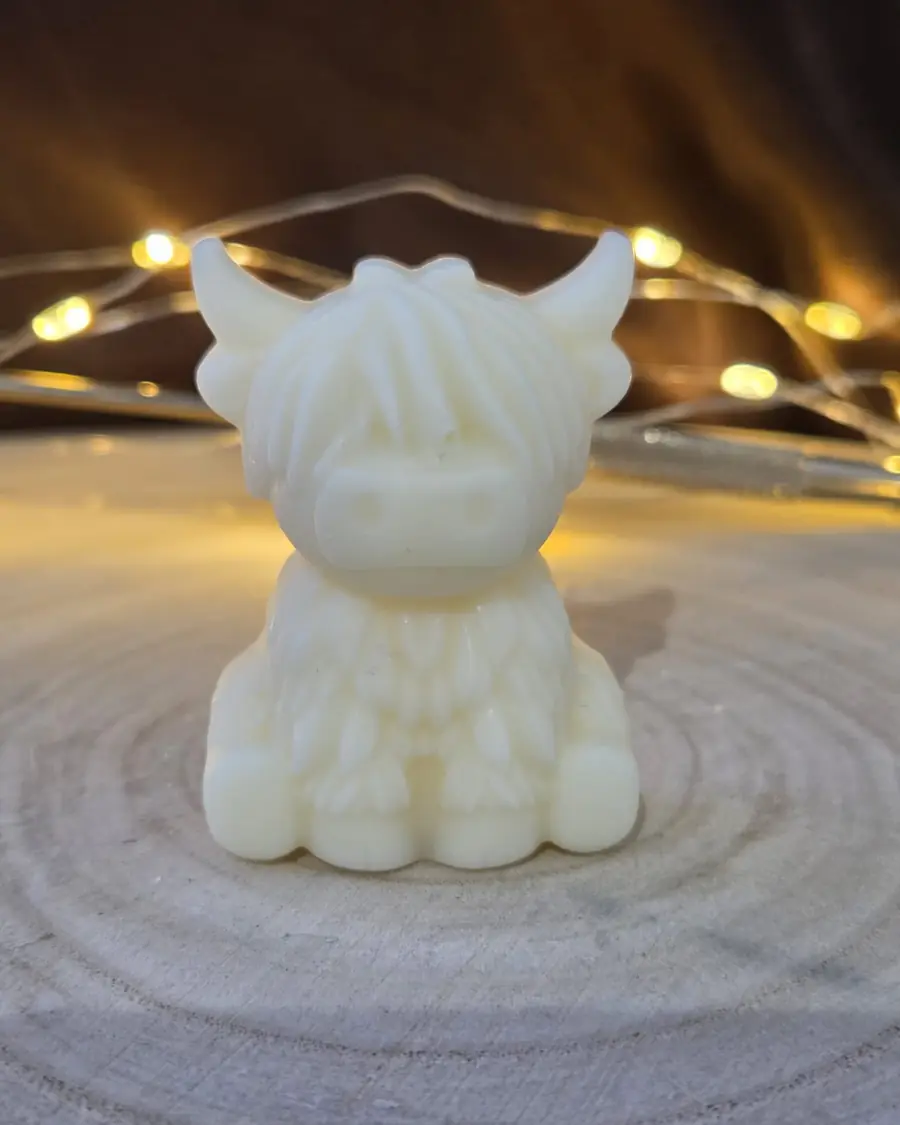 Small ivory Highland cow candle on a wood slice with fairy lights