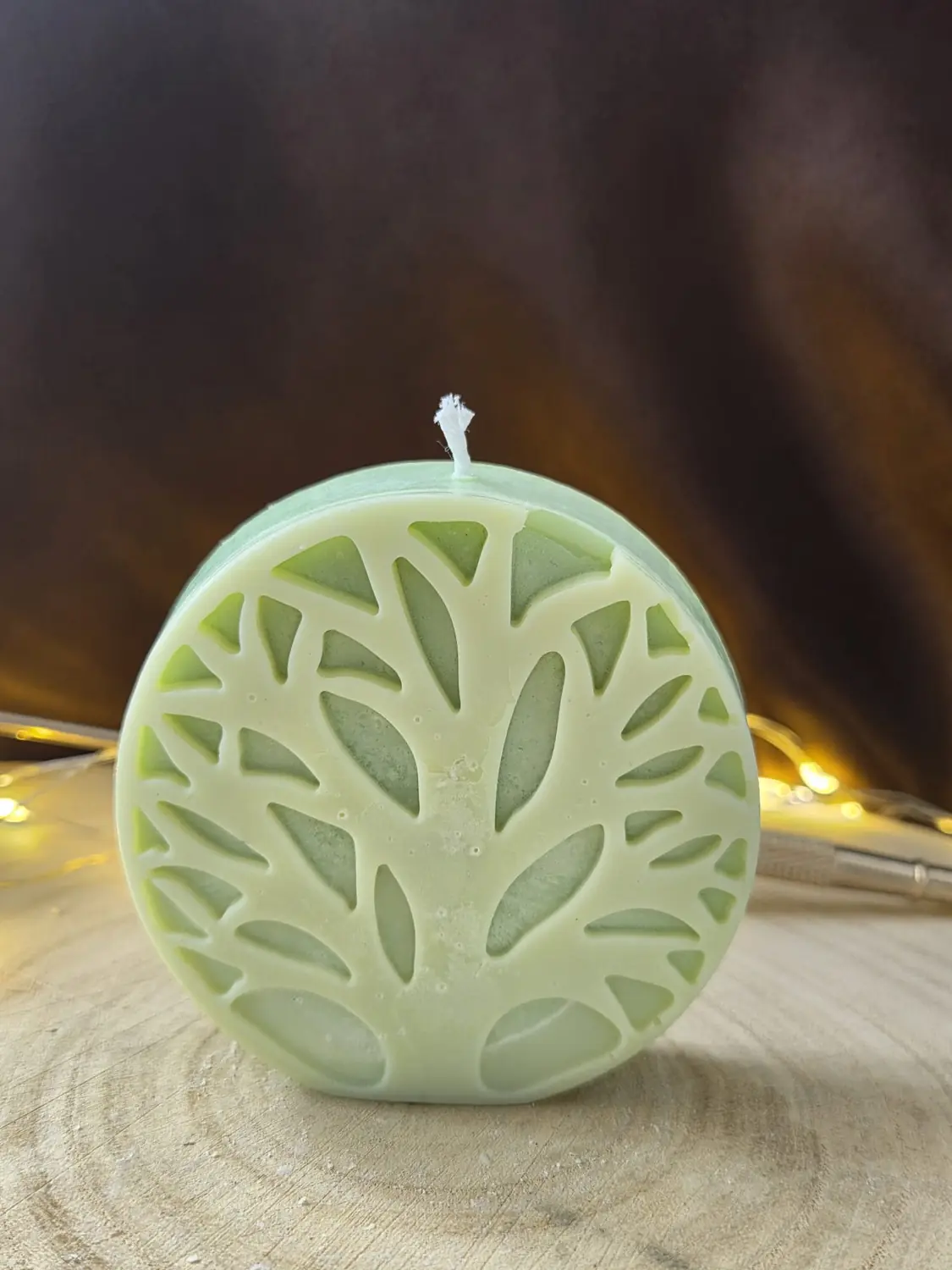 Pale green round candle with a tree of life in relief, fairy lights behind