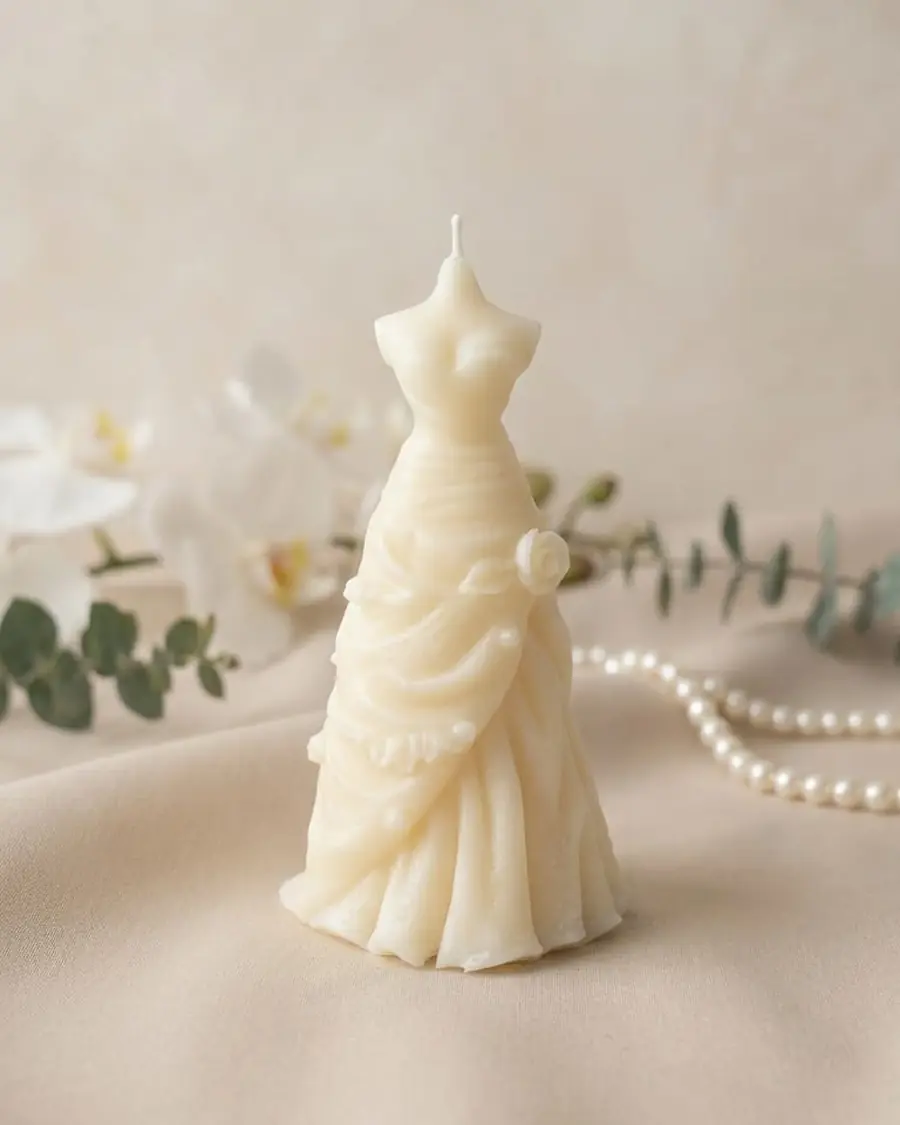Ivory wedding dress candle with draped flowers, beside pearls and eucalyptus