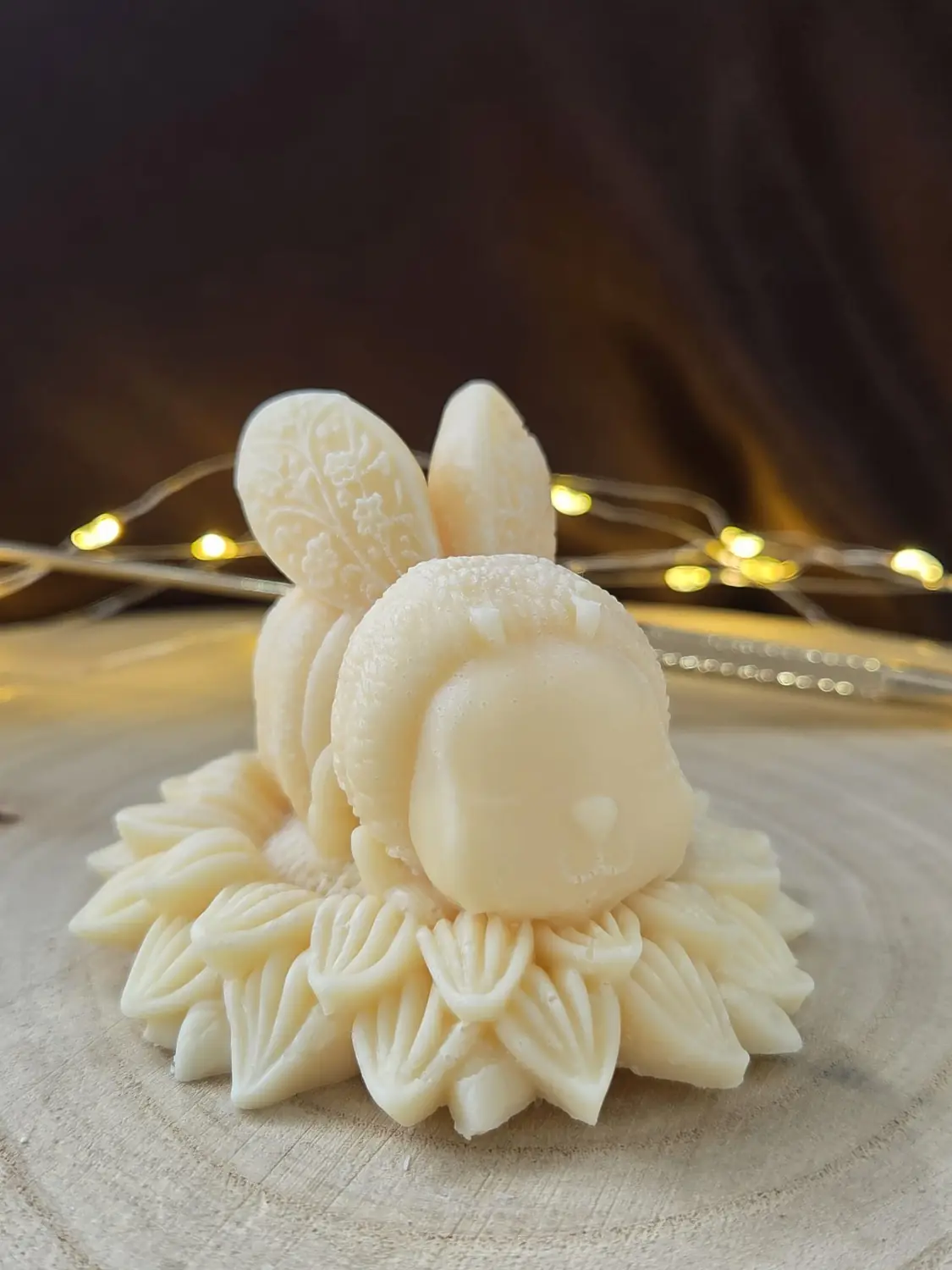 Ivory bee candle with patterned wings sitting on a ring of carved petals