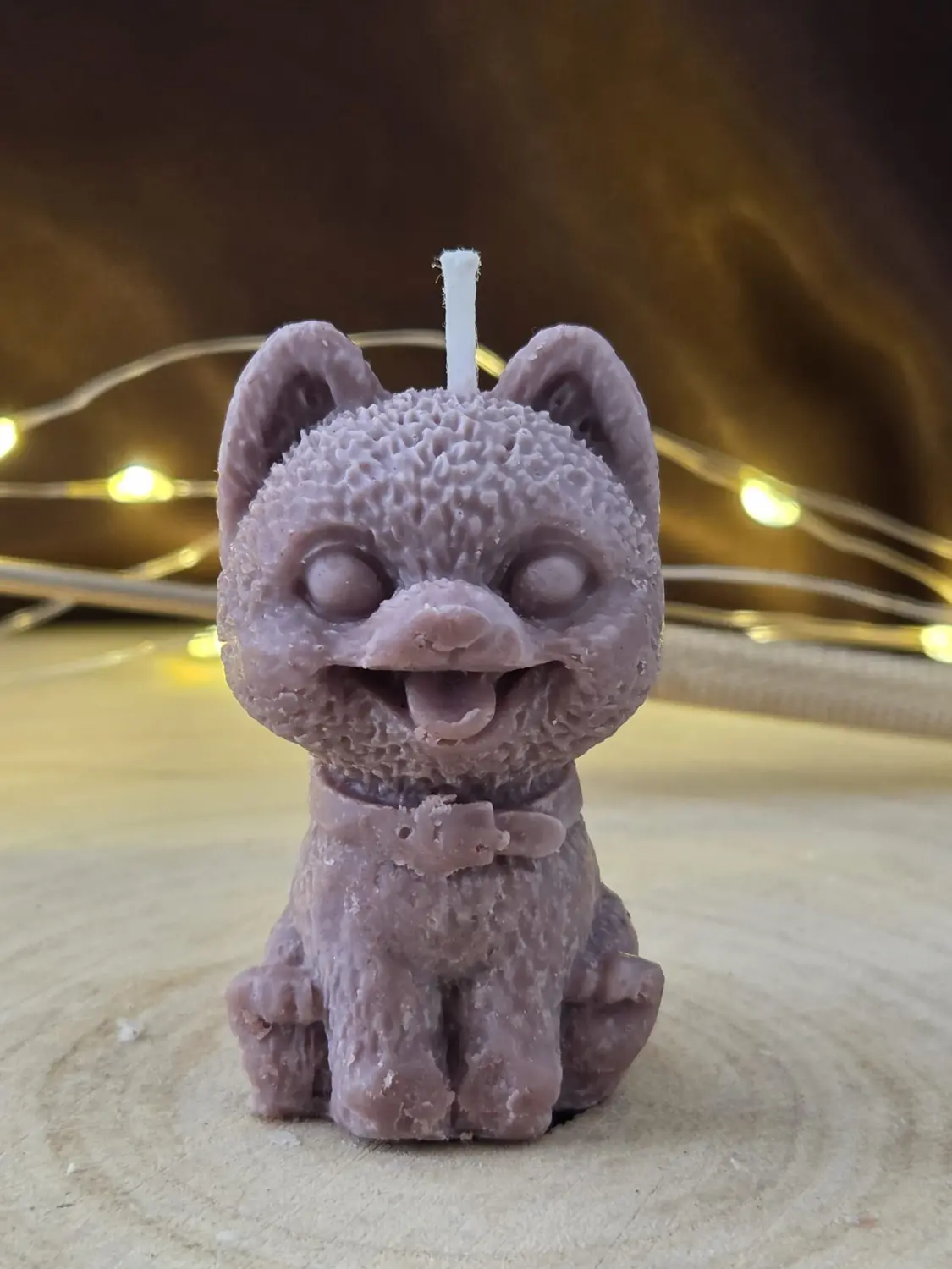 Mauve cat candle with its tongue out and a buckled collar, on a wood slice