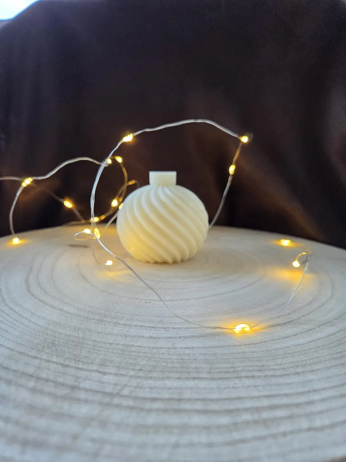 Ivory swirled bauble candle on a wood slice circled by fairy lights