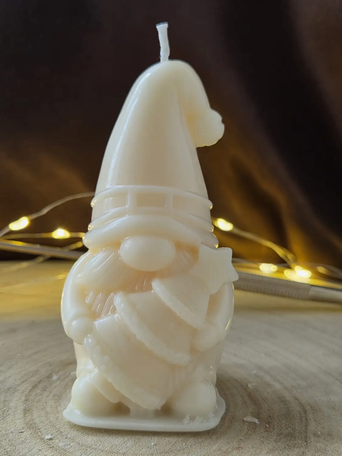Ivory gonk candle in a tall hat holding a small Christmas tree, fairy lights behind