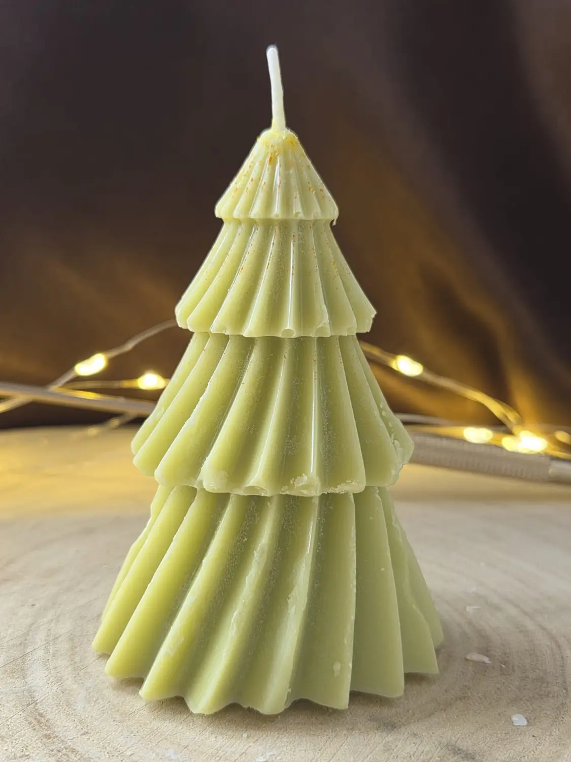 Green tiered Christmas tree candle, fairy lights glowing behind