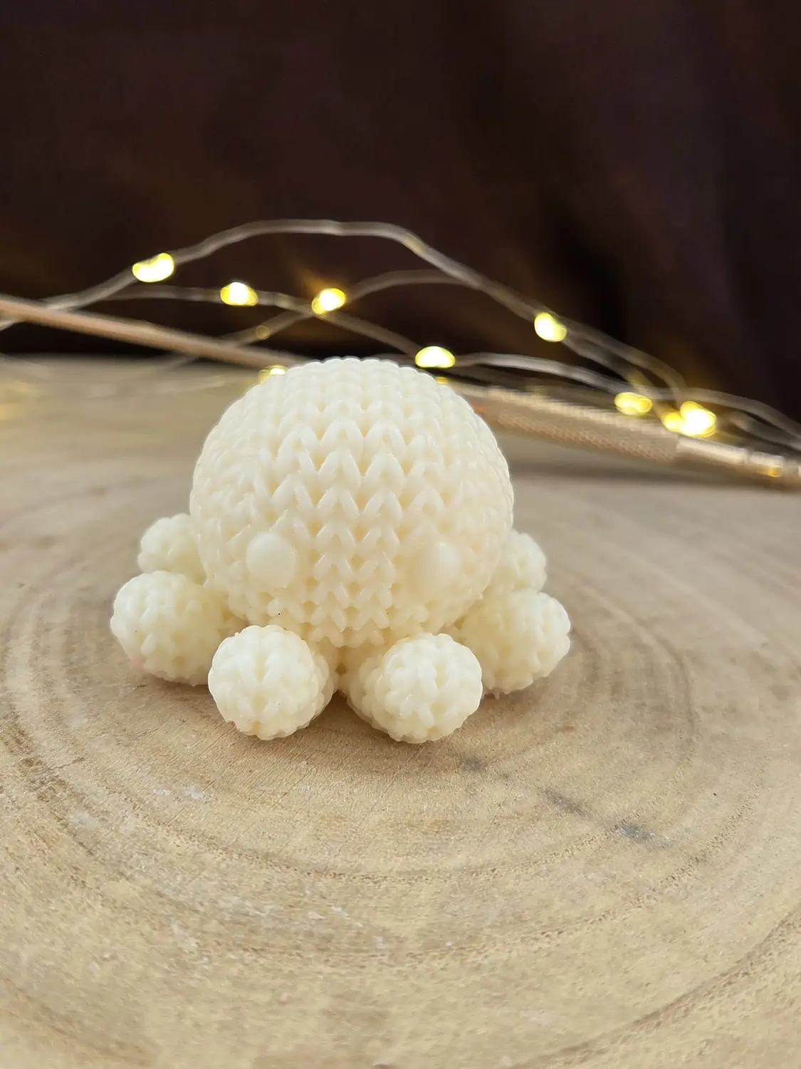 Ivory octopus candle with a knitted texture and bobble legs, on a wood slice