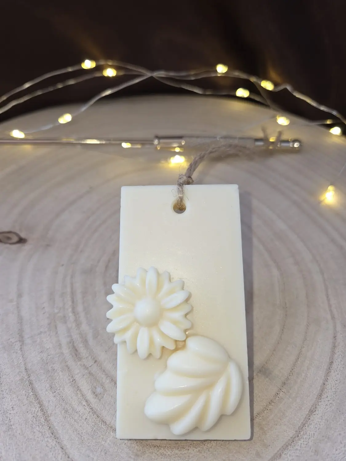Ivory wax tablet with a daisy and a leaf, hanging from a twine loop