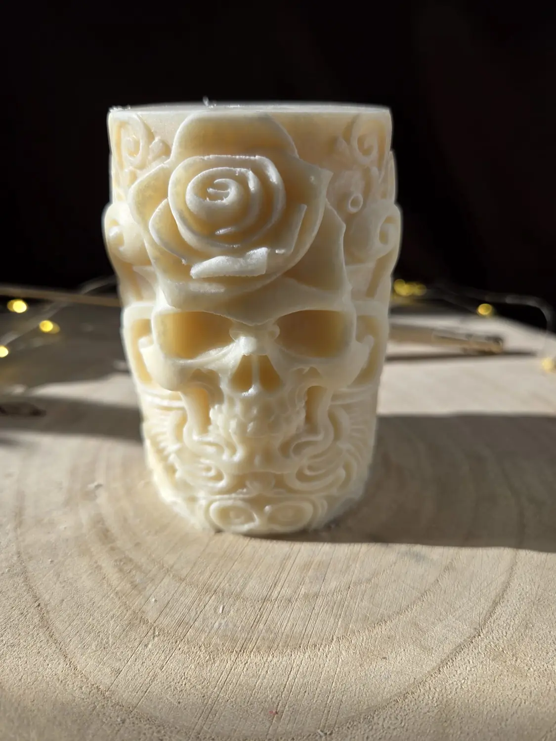 Ivory pillar candle carved with a skull beneath a rose, in low sunlight
