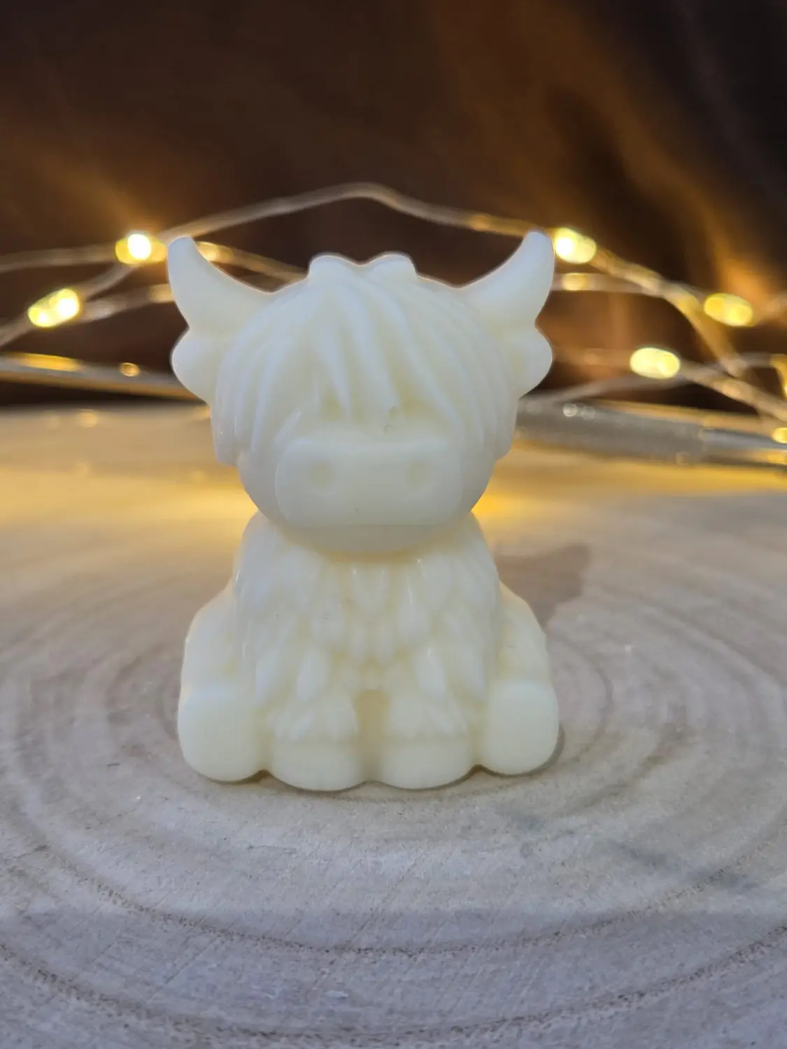 Small ivory Highland cow candle on a wood slice with fairy lights