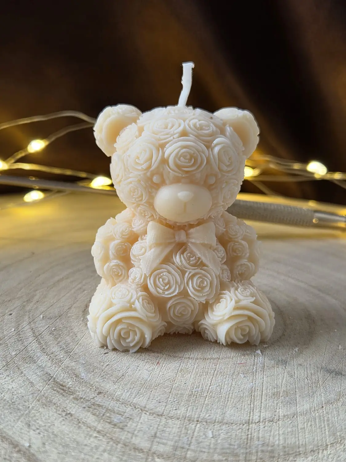 Ivory teddy bear candle covered in moulded roses with a bow, on a wood slice